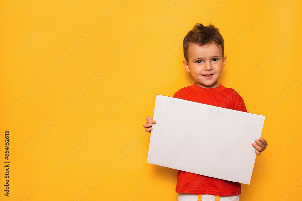 Studio portrait of a happy boy with a clean white poster in his hands on a bright yellow background, with a place for your text or advertising Studio portrait of a happy boy with a clean white poster in his hands on a bright yellow background, with a place for your text or advertising