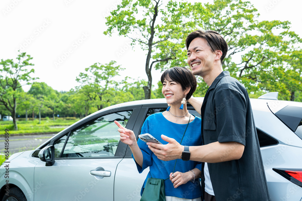 A couple smiling and looking at their smartphone next to a car.