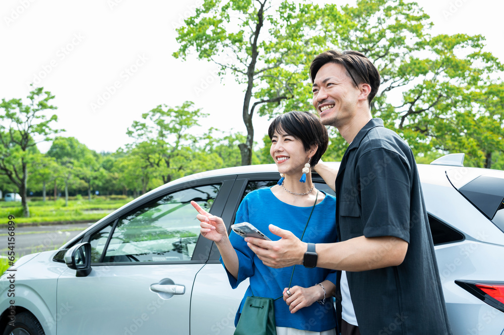 A couple smiling and looking at their smartphone next to a car. A couple smiling and looking at their smartphone next to a car.