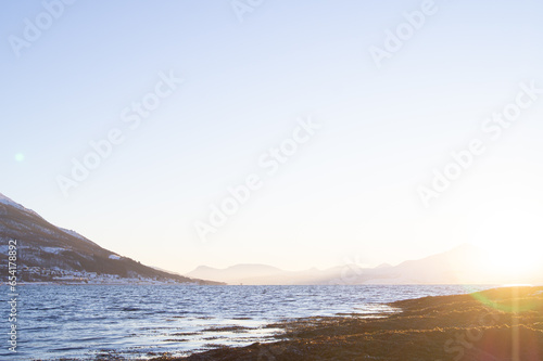 Evening, sundown, clear sky, last moments. In Tromso, Norway. Camera low. Fjord, sea, water. Mountain in background. Winter,