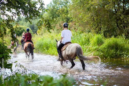 Horse ride, young girls riders, crossing a river on horseback. © наталья саксонова