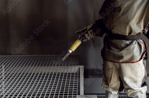 sandblasting a metal surface in a workshop close-up. a master in special clothing holds a sandblasting hose in his hands. working with sandblasting