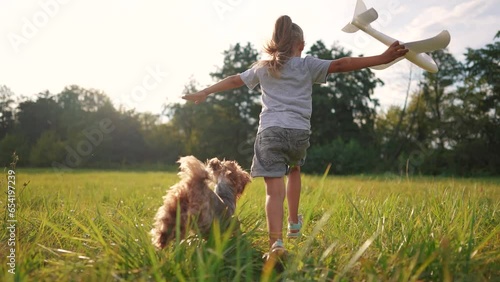 the girl runs with the plane and the dog. happy family kid dream concept. girl daughter running across a field of green grass in the park playing with a toy airplane and a pet lifestyle dog