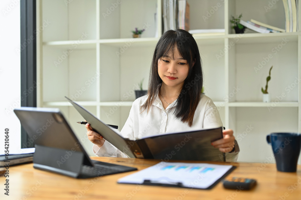 Concentrated asian female employee reviewing financial reports at her workplace Concentrated asian female employee reviewing financial reports at her workplace