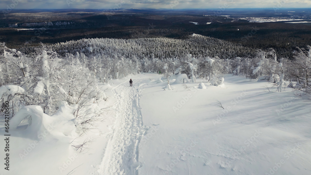 Top view of man walking into mountains in winter forest. Clip. Man goes on winter hike in mountains. Man walks alone uphill in winter in forest