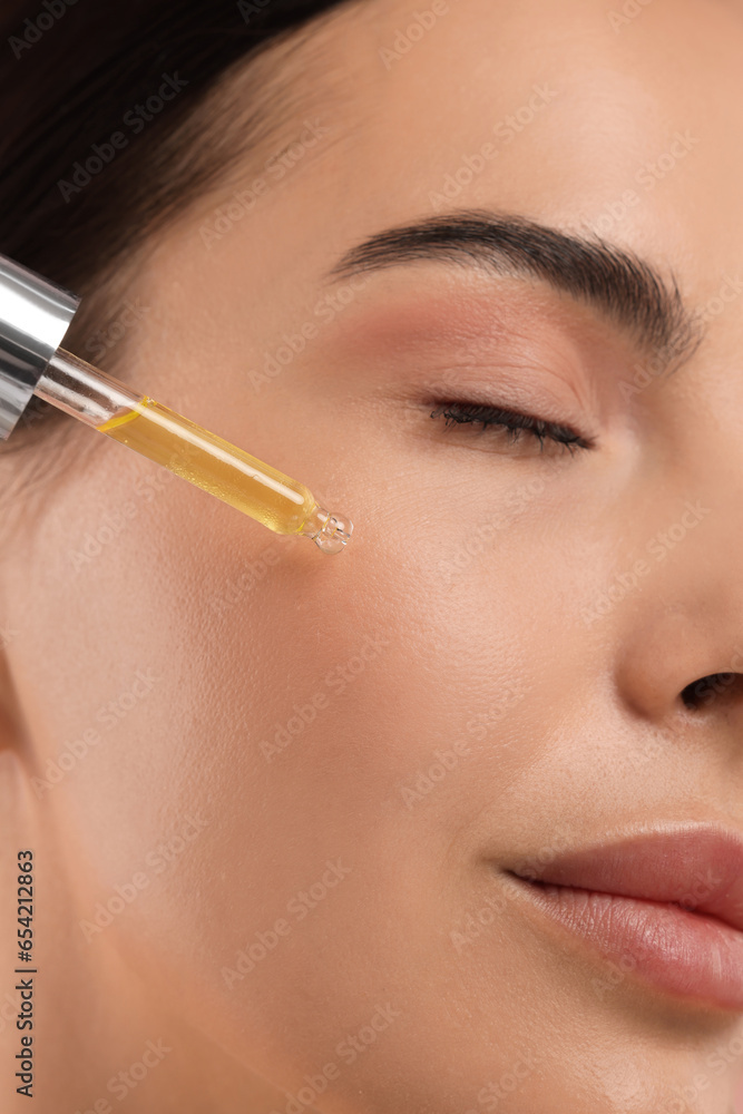 Beautiful young woman applying serum onto her face, closeup