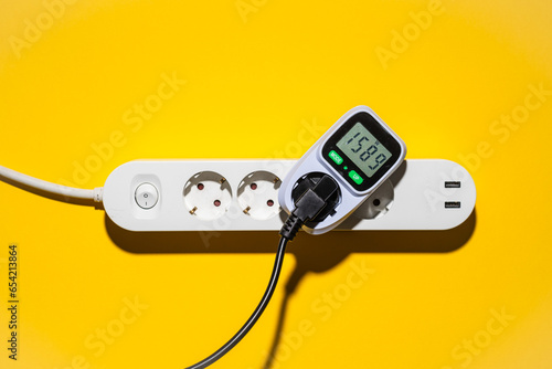 Top view auf ein Energiekosten Messgerät in einer Steckerleiste vor gelbem Hintergrund photo