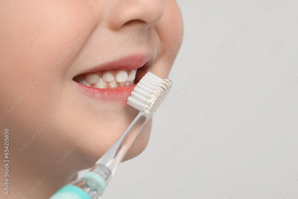 Cute little boy brushing his teeth with electric toothbrush on white background, closeup. Space for text