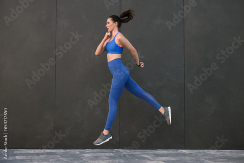 Beautiful woman in stylish sportswear jumping near black wall outdoors © New Africa