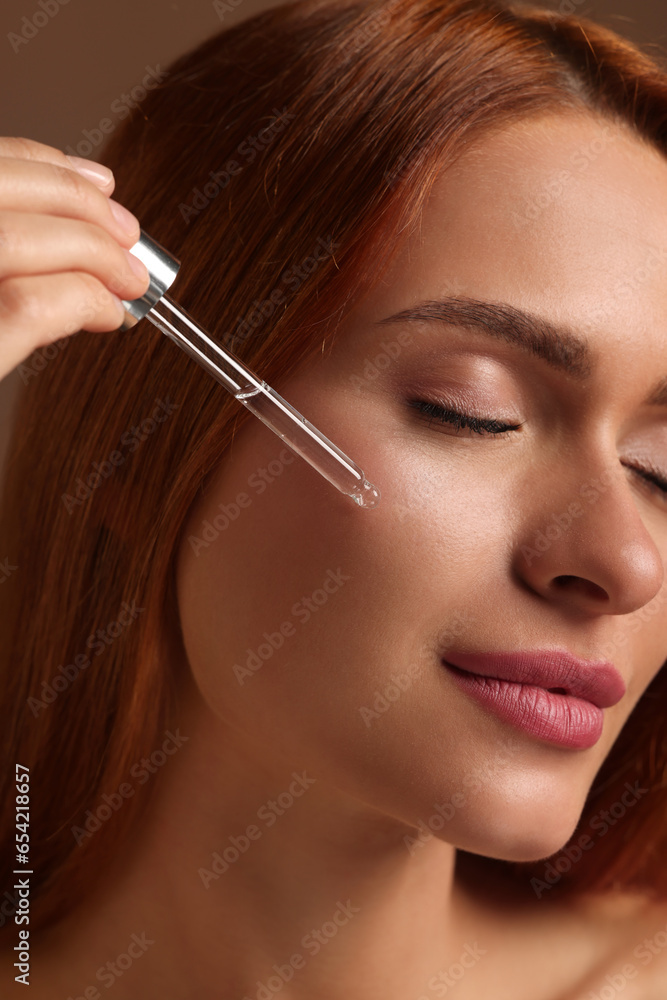 Beautiful young woman applying cosmetic serum onto her face on brown background, closeup Beautiful young woman applying cosmetic serum onto her face on brown background, closeup