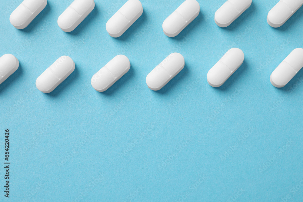 White pills on light blue background, flat lay. Space for text