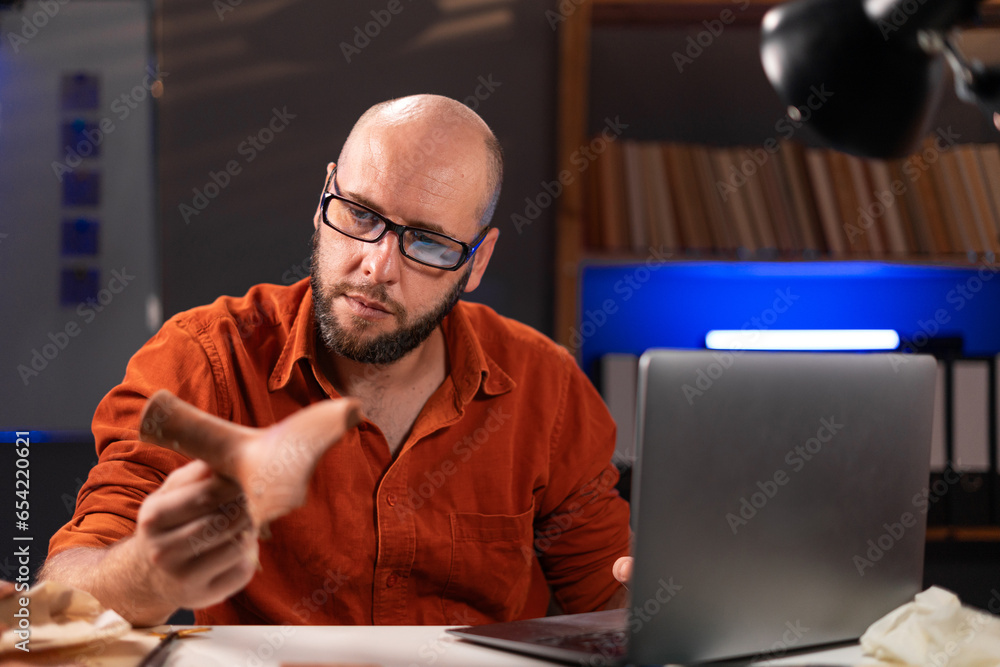 Archaeologist working late night in office studying artifacts online uses laptop computer Archaeologist working late night in office studying artifacts online uses laptop computer