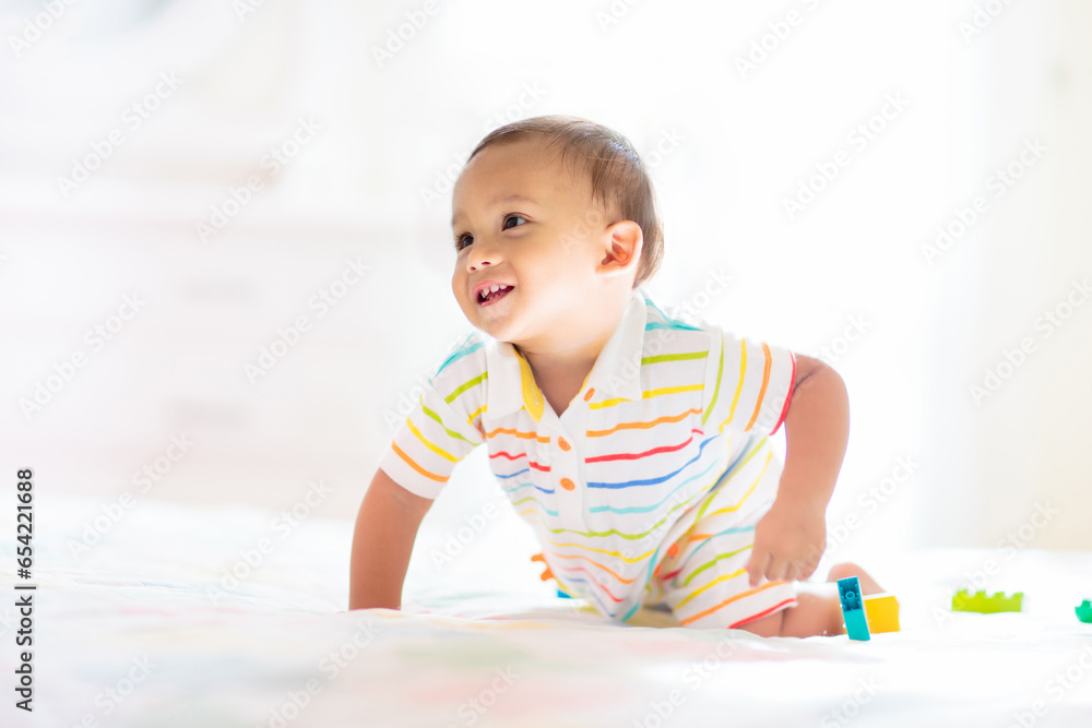 Baby boy playing on bed in sunny nursery Baby boy playing on bed in sunny nursery