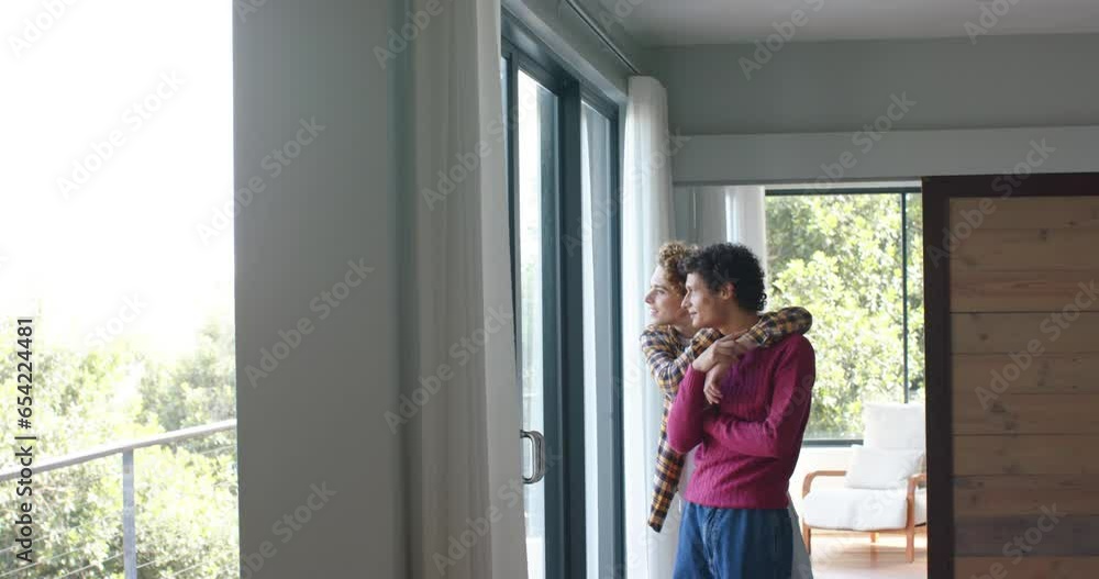 Happy diverse gay male couple looking through window and embracing at home, slow motion Happy diverse gay male couple looking through window and embracing at home, slow motion