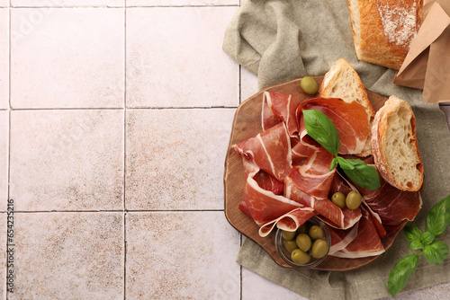 Φωτογραφία Slices of tasty cured ham, olives, bread and basil on tiled table, flat lay