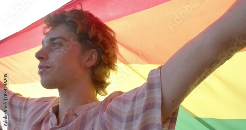 Portrait of happy caucasian man holding rainbow lgbt flag on balcony at home, slow motion