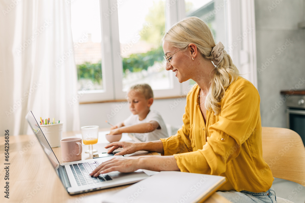 Side view of a businesswoman working on laptop with her child sitting next to her. Side view of a businesswoman working on laptop with her child sitting next to her.
