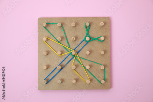 Wooden geoboard with dragonfly shape made of rubber bands on pink background, top view. Educational toy for motor skills development photo