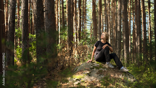 woman sits on a boulder in thicket of forest, idea of restoring health and relaxation, forest baths photo