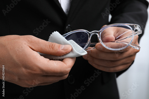 Man wiping glasses with microfiber cloth on light background  closeup