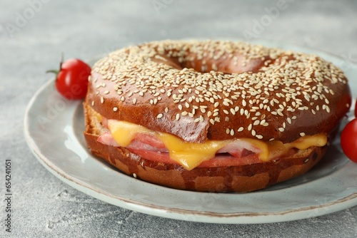 Delicious bagel with ham and cheese on light grey textured table, closeup