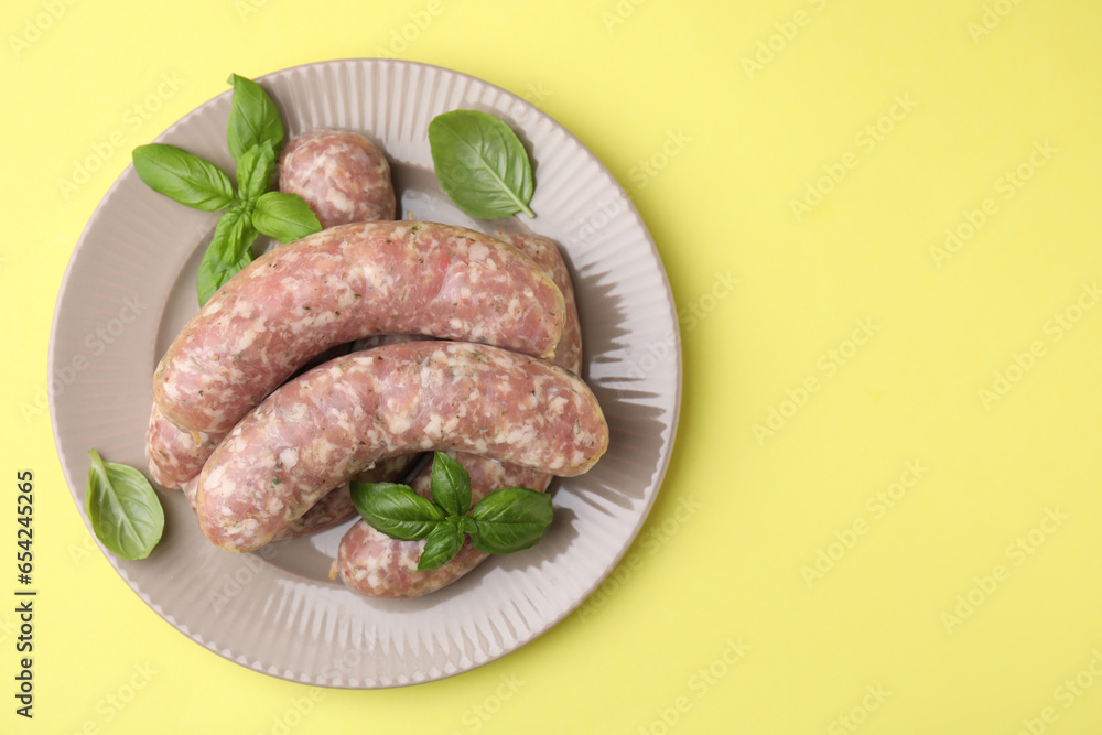 Raw homemade sausages and basil leaves on yellow background, top view. Space for text