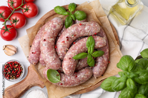 Raw homemade sausages, basil leaves, tomatoes and spices on white table, flat lay