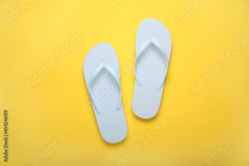 Stylish white flip flops on yellow background  top view