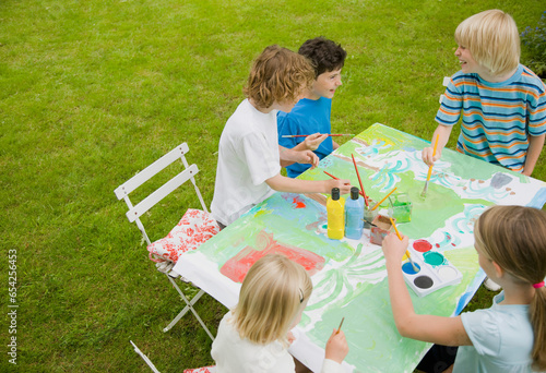 Children sitting and painting in the garden
 photo