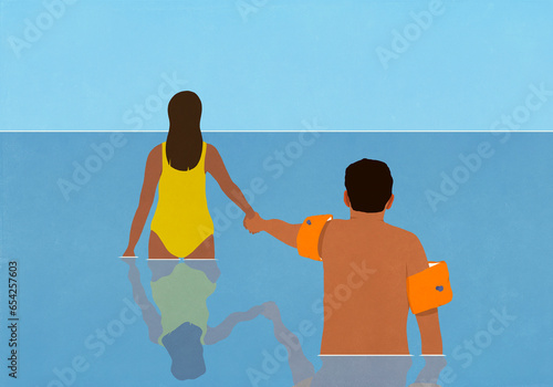 Wife holding hands with hesitant husband in water wings, wading in ocean water
 photo