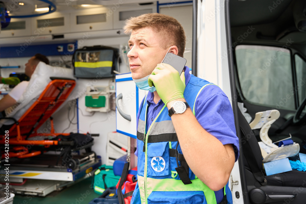 Paramedic communicates on a mobile phone near an ambulance Paramedic communicates on a mobile phone near an ambulance