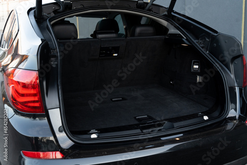 Black luxury auto with capacious open trunk standing outdoors. Empty space for goods transportation. Quality details and interior of modern auto.