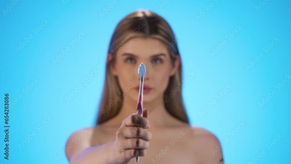 Static medium shot of a young beautiful woman or model holding a toothbrush for good and important dental care and dental health into the camera in front of blue background in slow motion Static medium shot of a young beautiful woman or model holding a toothbrush for good and important dental care and dental health into the camera in front of blue background in slow motion