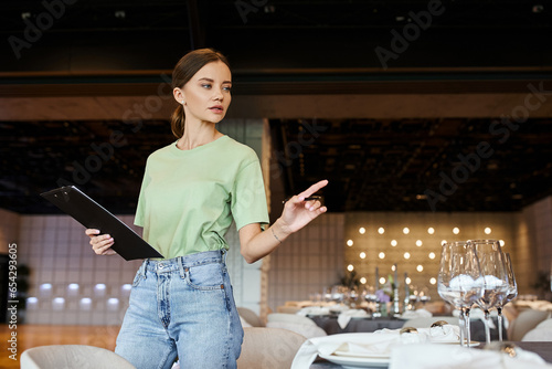 Valokuva event coordinator with clipboard pointing with pen at table with festive setting
