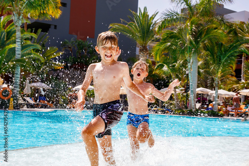 Two happy little kid boys jumping in the pool and having fun on family vacations in a hotel resort. Children playing in water with a water gun. Laughing running siblings brothers and best friends photo