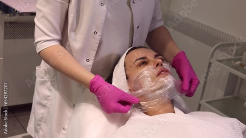 Cosmetologist applying cream with anesthesia on patient's face, portrait closeup view. Preparing skin for biorevitalization or thread lifting procedure. Woman in beauty clinic with doctor beautician.