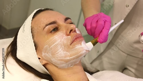 Cosmetologist applying cream with anesthesia on patient's face, portrait closeup view. Preparing skin for biorevitalization or thread lifting procedure. Woman in beauty clinic with doctor beautician.