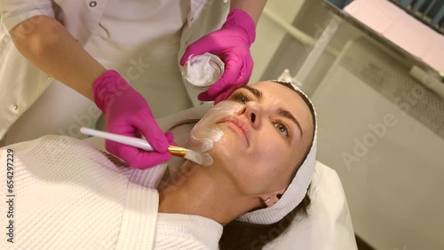 Cosmetologist applying cream with anesthesia on patient's face, portrait closeup view. Preparing skin for biorevitalization or thread lifting procedure. Woman in beauty clinic with doctor beautician.