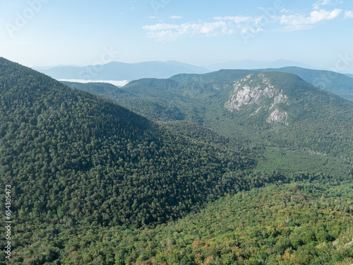 A summertime mountainous landscape of the White Mountains in New Hampshire. The rounded summits and sharp cliffs of these peaks make the lush green forest magical. Clear blue skies in the background. photo