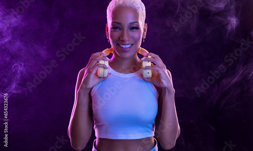 Hipster fashion girl, african american model wear headphones enjoy listen new cool music mix. Woman stand at purple studio background in trendy club purple party light with fog.