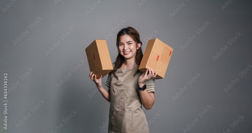 Young asian woman startup small business freelance holding parcel box standing isolated on grey background, Online marketing packing box delivery concept Young asian woman startup small business freelance holding parcel box standing isolated on grey background, Online marketing packing box delivery concept
