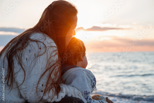 Mom and son are sitting on the seashore. The mother hugs the child. Happy childhood. Sunset in the sea.