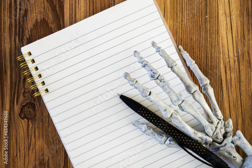 skeleton hand holding black pen on a blank lined notebook mock up