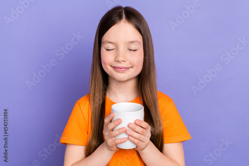 Photo of little schoolgirl closed eyes relax enjoy drinking sweet tea cup good mood wear orange t shirt isolated on violet color background