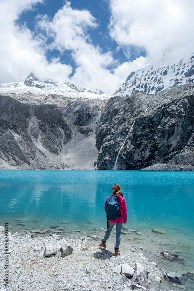 A girl by a turquoise lagoon wearing a pink jacket with a waterfall in the background A girl by a turquoise lagoon wearing a pink jacket with a waterfall in the background