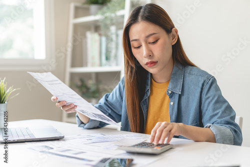 Young Asian woman looking at credit card invoice in her hands and worry about cash on bills payday photo