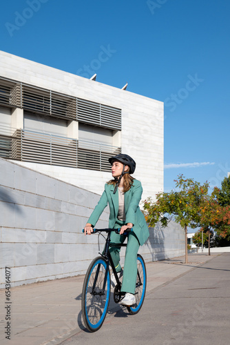 Stylish business woman in green suit and helmet riding her bicycle at the financial district with modern building on the background photo