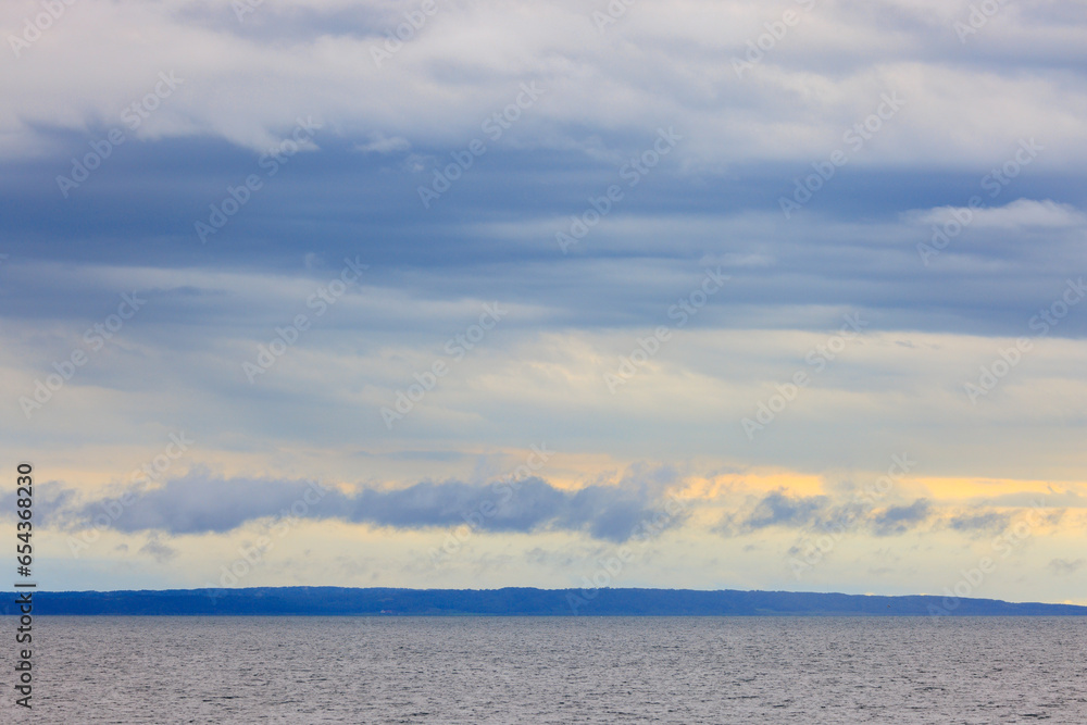 Early morning clouds over distant land, viewed offshore in calm ocean Early morning clouds over distant land, viewed offshore in calm ocean