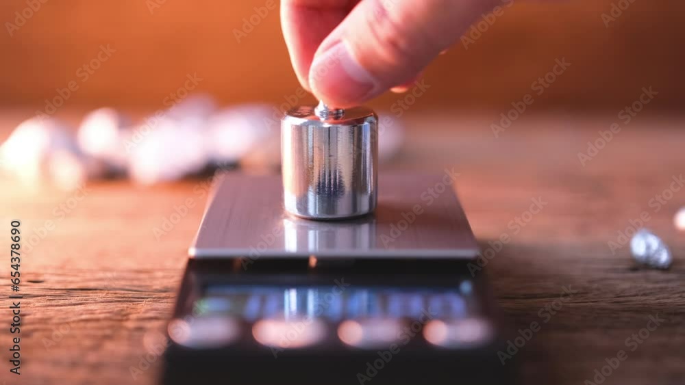 man's hand is placing a standard calibration weight on a weighing scale