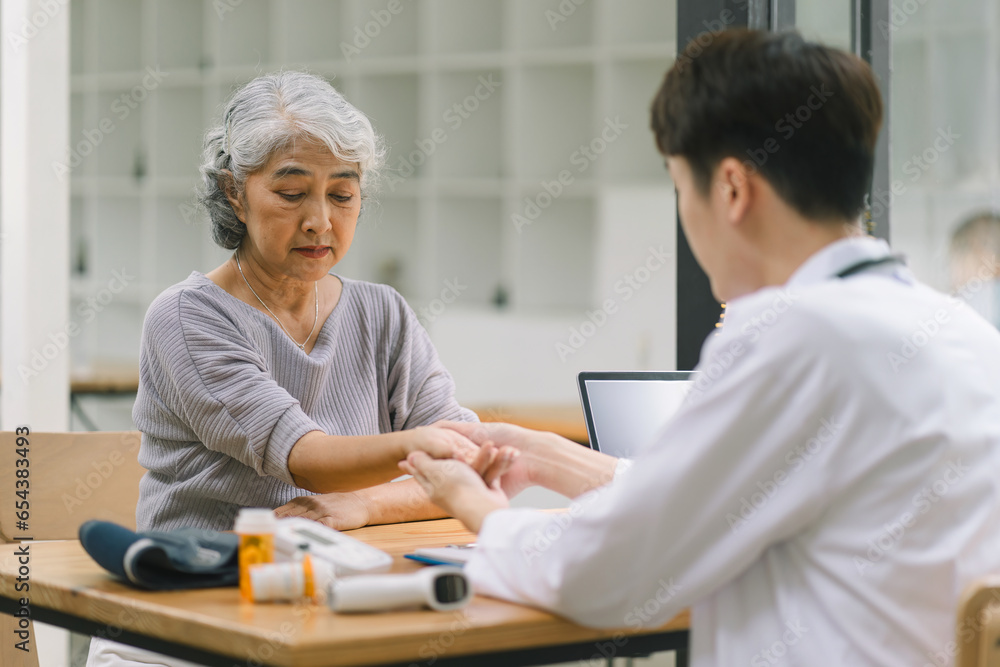 Obraz premium A young doctor using digital tonometer check blood pressure for senior woman. A doctor is holding a senior woman's hand.